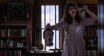 Movie still from “Beetlejuice” (1988), directed by Tim Burton – A woman holding up a mask of a man with glasses; Medium shot, Low angle