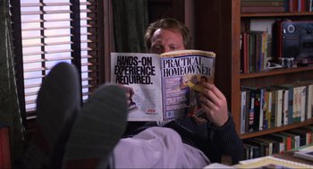 Movie still from “Beetlejuice” (1988), directed by Tim Burton – A man is reading a magazine while sitting in a chair; Medium shot, High angle