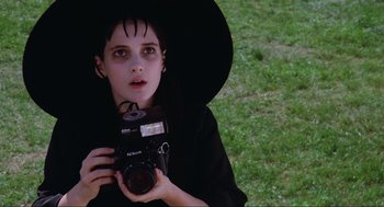 Movie still from “Beetlejuice” (1988), directed by Tim Burton – A young girl dressed as a witch holding a camera; Close Up shot, High angle
