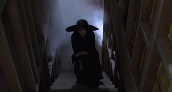 Movie still from “Beetlejuice” (1988), directed by Tim Burton – A woman dressed as a witch walking down a staircase; Medium shot, Low angle