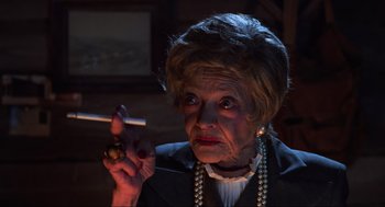 Movie still from “Beetlejuice” (1988), directed by Tim Burton – An older woman holding a cigarette in her hand; Close Up shot, Over the shoulder angle