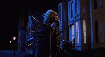 Movie still from “Beetlejuice” (1988), directed by Tim Burton – A person in a costume holding a bunch of knives; Medium shot, Low angle