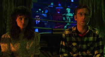 Movie still from “Beetlejuice” (1988), directed by Tim Burton – A man and a woman sitting next to each other in front of a screen; Medium shot, Over the shoulder angle
