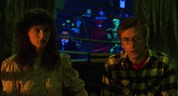 Movie still from “Beetlejuice” (1988), directed by Tim Burton – A man and a woman sitting next to each other in front of a screen; Medium shot, Low angle