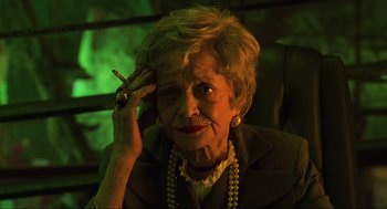 Movie still from “Beetlejuice” (1988), directed by Tim Burton – An older woman smoking a cigarette while holding a cell phone to her ear; Close Up shot, High angle