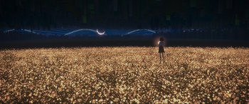 A girl is standing in a field with lights in the background