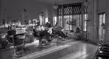 Movie still from “The Man Who Wasn't There” (2001), directed by Joel Coen – A couple of men sitting in barber chairs in a room; Wide shot, Low angle