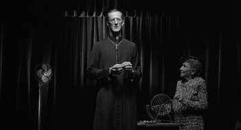Movie still from “The Man Who Wasn't There” (2001), directed by Joel Coen – A man dressed as a priest standing next to a woman; Medium shot, Low angle