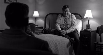 Movie still from “The Man Who Wasn't There” (2001), directed by Joel Coen – A black and white photo of an older man sitting on a bed; Medium shot, Over the shoulder angle