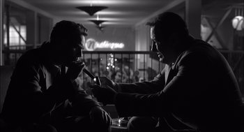 Movie still from “The Man Who Wasn't There” (2001), directed by Joel Coen – Two men sitting at a table in front of a neon sign; Medium shot, Low angle