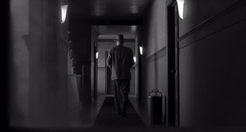 Movie still from “The Man Who Wasn't There” (2001), directed by Joel Coen – A man walking down a hall way with a suitcase; Wide shot, Low angle