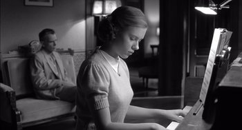 Movie still from “The Man Who Wasn't There” (2001), directed by Joel Coen – A woman is playing a piano in a living room; Medium shot, Low angle