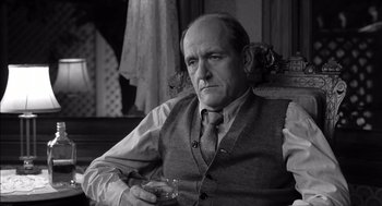 Movie still from “The Man Who Wasn't There” (2001), directed by Joel Coen – An older man sitting in a chair holding a glass; Close Up shot, Over the shoulder angle