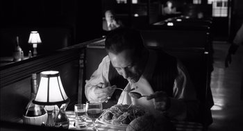 Movie still from “The Man Who Wasn't There” (2001), directed by Joel Coen – A black and white photo of a man eating a meal; Medium shot, High angle