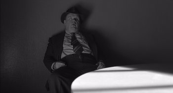 Movie still from “The Man Who Wasn't There” (2001), directed by Joel Coen – A black and white photo of a man in a suit and hat; Medium shot, High angle