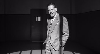 Movie still from “The Man Who Wasn't There” (2001), directed by Joel Coen – A man in a suit standing in front of a door; Medium shot, Low angle