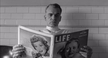 Movie still from “The Man Who Wasn't There” (2001), directed by Joel Coen – An older man reading a magazine in a bathroom; Close Up shot, Low angle