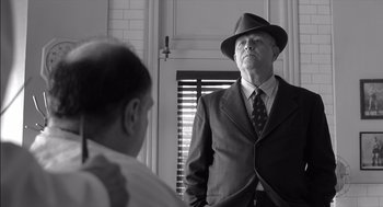 Movie still from “The Man Who Wasn't There” (2001), directed by Joel Coen – An older man in a suit and hat looking at a younger man in a hat; Medium shot, Low angle