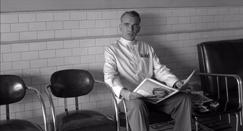 Movie still from “The Man Who Wasn't There” (2001), directed by Joel Coen – A black and white photo of a man sitting on a chair; Close Up shot, Low angle