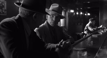 Movie still from “The Man Who Wasn't There” (2001), directed by Joel Coen – A black and white photo of a man wearing a hat; Medium shot, Over the shoulder angle