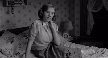 Movie still from “The Man Who Wasn't There” (2001), directed by Joel Coen – A woman sitting on top of a bed in front of a lamp; Medium shot, Low angle