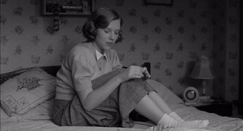 Movie still from “The Man Who Wasn't There” (2001), directed by Joel Coen – A woman sitting on a bed looking at her phone; Medium shot, Low angle