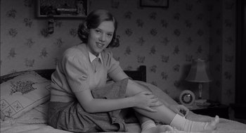 Movie still from “The Man Who Wasn't There” (2001), directed by Joel Coen – A young woman sitting on a bed in a room; Medium shot, Low angle