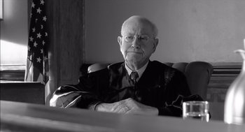 Movie still from “The Man Who Wasn't There” (2001), directed by Joel Coen – An older man in a robe and glasses sitting at a desk; Close Up shot, Over the shoulder angle