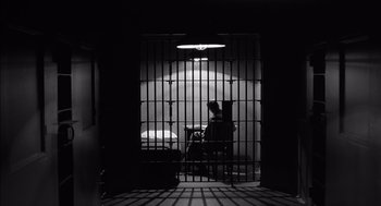 Movie still from “The Man Who Wasn't There” (2001), directed by Joel Coen – A man sitting in a jail cell in a dark room; Wide shot, Low angle