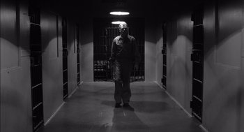 Movie still from “The Man Who Wasn't There” (2001), directed by Joel Coen – A man standing in a dark room with a mask on; Wide shot, Low angle