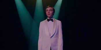 Movie still from “Better Nate Than Ever” (2022), directed by Tim Federle – A man in a white tuxedo standing in front of green lights; Medium shot, Low angle