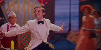 Movie still from “Better Nate Than Ever” (2022), directed by Tim Federle – A man in a white tuxedo sitting on a chair; Medium shot, Over the shoulder angle