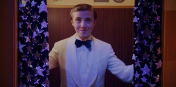 Movie still from “Better Nate Than Ever” (2022), directed by Tim Federle – A young man in a white suit and a bow tie; Medium shot, Low angle