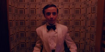 Movie still from “Better Nate Than Ever” (2022), directed by Tim Federle – A man in a white suit and black bow tie; Medium shot, Low angle