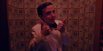 Movie still from “Better Nate Than Ever” (2022), directed by Tim Federle – A man in a white suit and bow tie giving two thumbs up; Close Up shot, High angle
