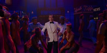 Movie still from “Better Nate Than Ever” (2022), directed by Tim Federle – A man in a white tuxedo surrounded by dancers; Medium shot, Over the shoulder angle