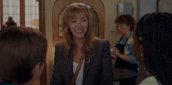 Movie still from “Better Nate Than Ever” (2022), directed by Tim Federle – A woman in a suit smiling for the camera; Close Up shot, Over the shoulder angle