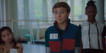 Movie still from “Better Nate Than Ever” (2022), directed by Tim Federle – A young man wearing a vest with the number 1 3 on it; Close Up shot, Over the shoulder angle