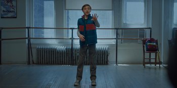 Movie still from “Better Nate Than Ever” (2022), directed by Tim Federle – A man standing on a dance floor with a red and blue striped vest; Medium shot, Low angle