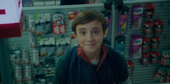 Movie still from “Better Nate Than Ever” (2022), directed by Tim Federle – A young boy is smiling for the camera in a store; Close Up shot, Over the shoulder angle