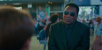 Movie still from “Better Nate Than Ever” (2022), directed by Tim Federle – A man in a suit and sunglasses looking at a crowd; Medium shot, Over the shoulder angle
