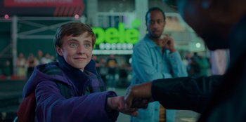 Movie still from “Better Nate Than Ever” (2022), directed by Tim Federle – A young boy is shaking hands with an older man; Medium shot, Over the shoulder angle