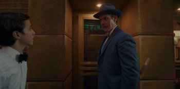 Movie still from “Better Nate Than Ever” (2022), directed by Tim Federle – A man in a suit and a hat standing in an elevator; Medium shot, Low angle