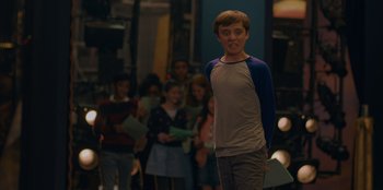 Movie still from “Better Nate Than Ever” (2022), directed by Tim Federle – A young man standing in front of a group of people; Medium shot, Over the shoulder angle
