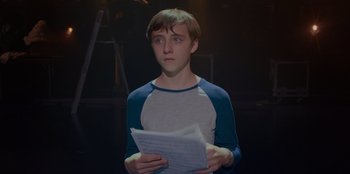 Movie still from “Better Nate Than Ever” (2022), directed by Tim Federle – A young man holding a piece of paper in his hands; Medium shot, Over the shoulder angle