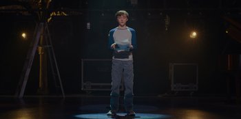 Movie still from “Better Nate Than Ever” (2022), directed by Tim Federle – A young man standing in the middle of a stage; Wide shot, Over the shoulder angle