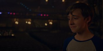 Movie still from “Better Nate Than Ever” (2022), directed by Tim Federle – A young boy standing in front of lights at night; Close Up shot, Over the shoulder angle