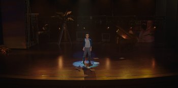 Movie still from “Better Nate Than Ever” (2022), directed by Tim Federle – A man standing on a stage in front of palm trees; Extreme Wide shot, High angle