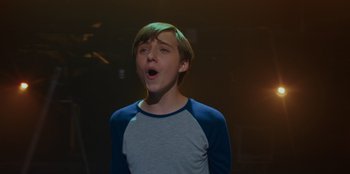 Movie still from “Better Nate Than Ever” (2022), directed by Tim Federle – A young man is singing in a dark room; Close Up shot, Over the shoulder angle