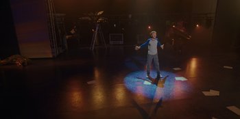 Movie still from “Better Nate Than Ever” (2022), directed by Tim Federle – A man standing on a stage with a microphone; Wide shot, High angle